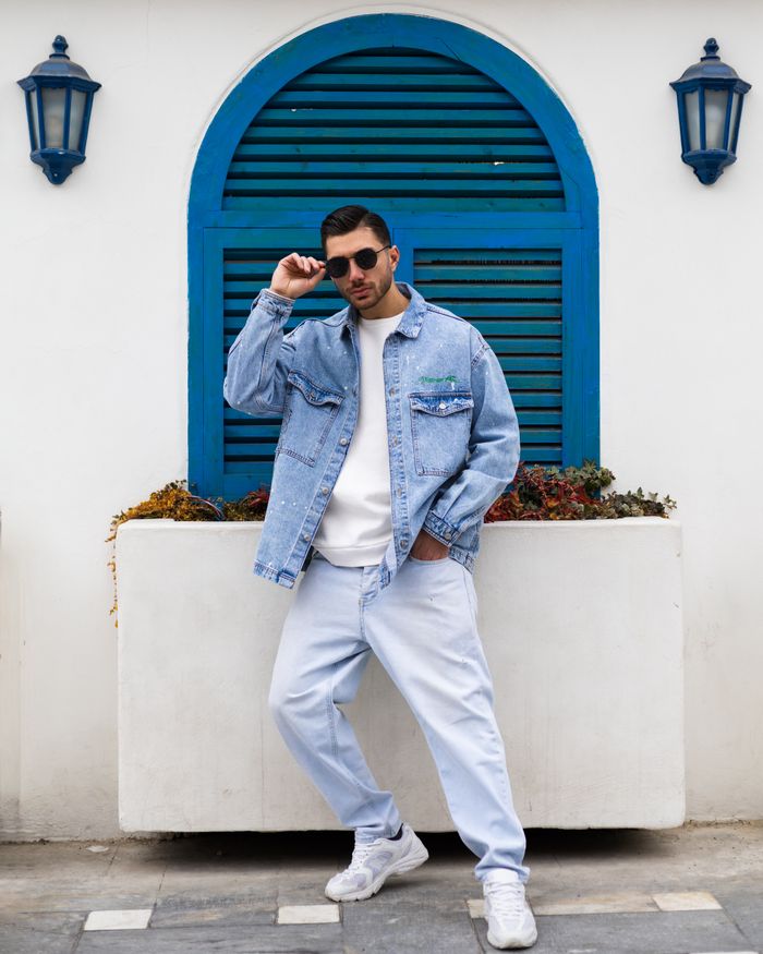 Fashionable man in denim ensemble posing outdoors against a vibrant blue arch.