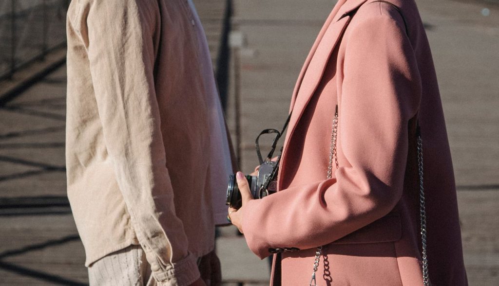 Stylish man and woman outdoors holding a camera, showcasing modern fashion trends.