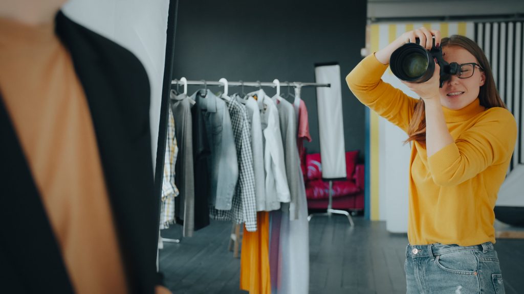 Female photographer taking pictures of a model in a stylish studio setting.